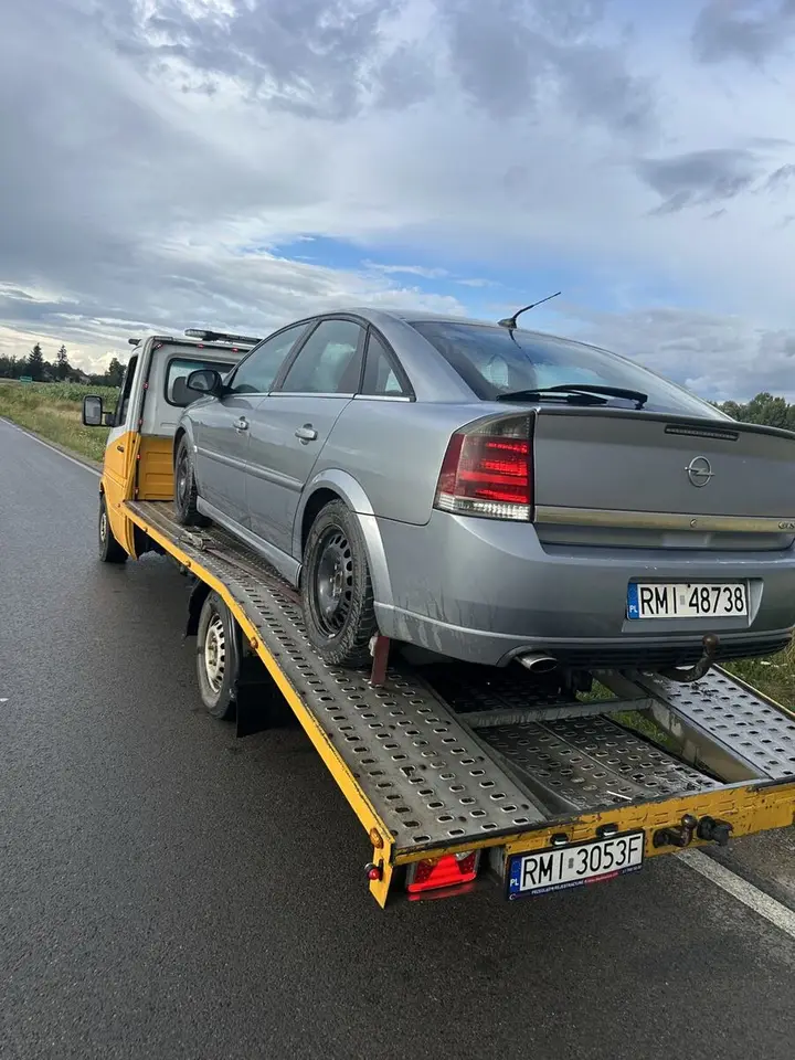 Laweta z szarym autem na platformie, zatrzymana na drodze.